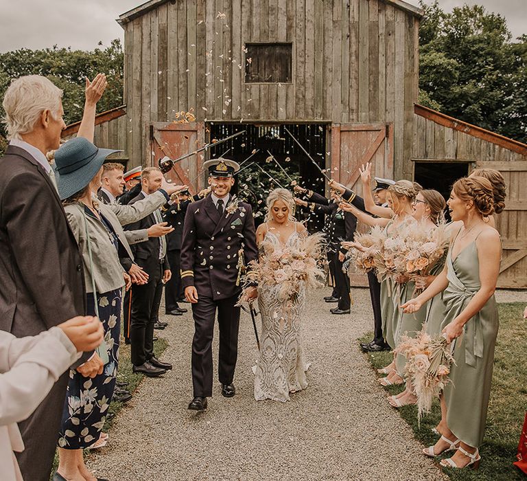 Groom in double breasted military uniform with white hat with bride in a boho gown walking as confetti is thrown over  