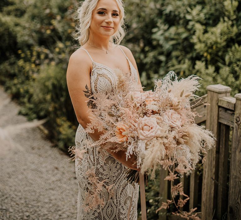 Bride in a boho lace wedding dress holding a pampas grass bouquet with bunny grass and blush pink roses 