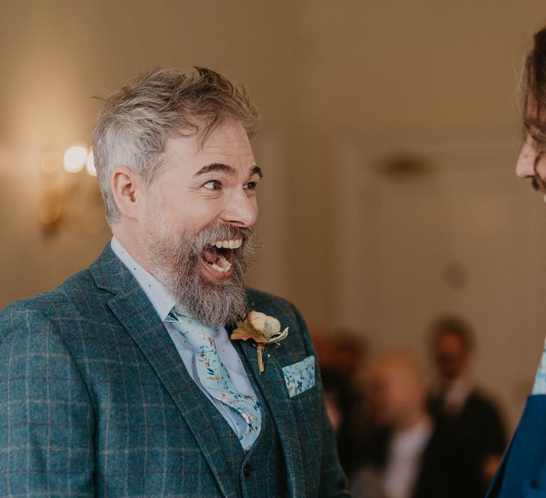 Groom wears three piece tartan suit complete with floral tie and matching pocket square alongside floral buttonhole 