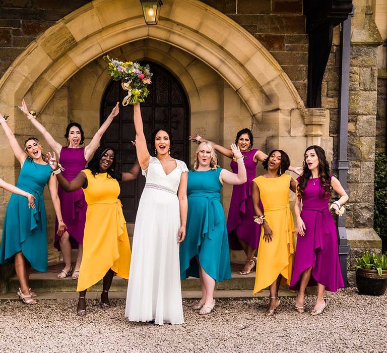 Bride stands with her bridesmaids who wear colourful bridesmaid dresses in purple, teal and yellow