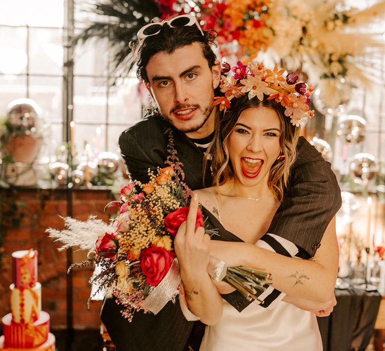 Bride in v-neck satin wedding dress and artistic flower crown and groom in dark grey pinstripe suit at grunge glam wedding 