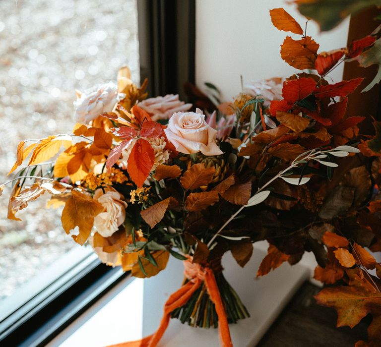 Burnt orange bridal bouquet complete with green foliage and tied with raw edge ribbon 