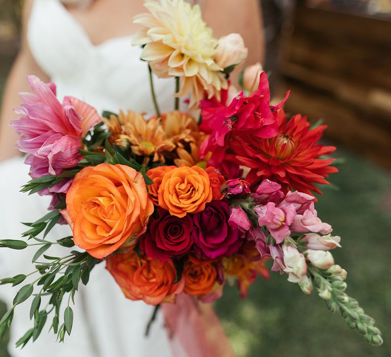 Bride carries tropical bridal bouquet complete with red and pink roses and green foliage 