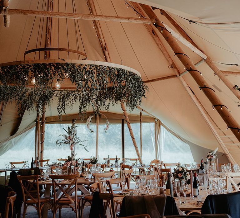 Floral installation hangs from light in tipi wedding reception 