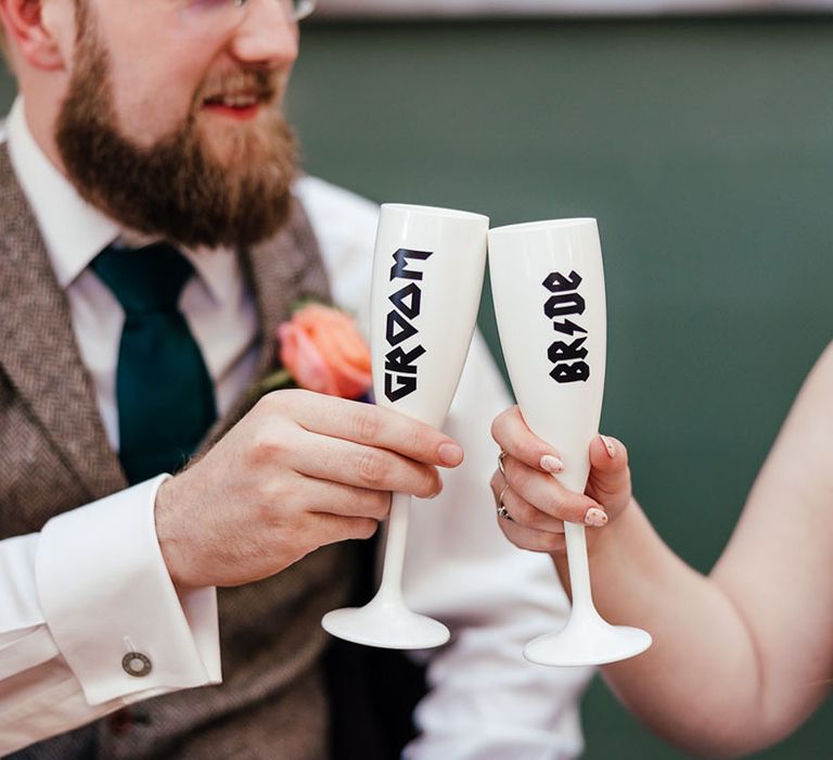 Bride and groom cheers-ing their white personalised champagne glasses with "bride" and "groom" black lettering 