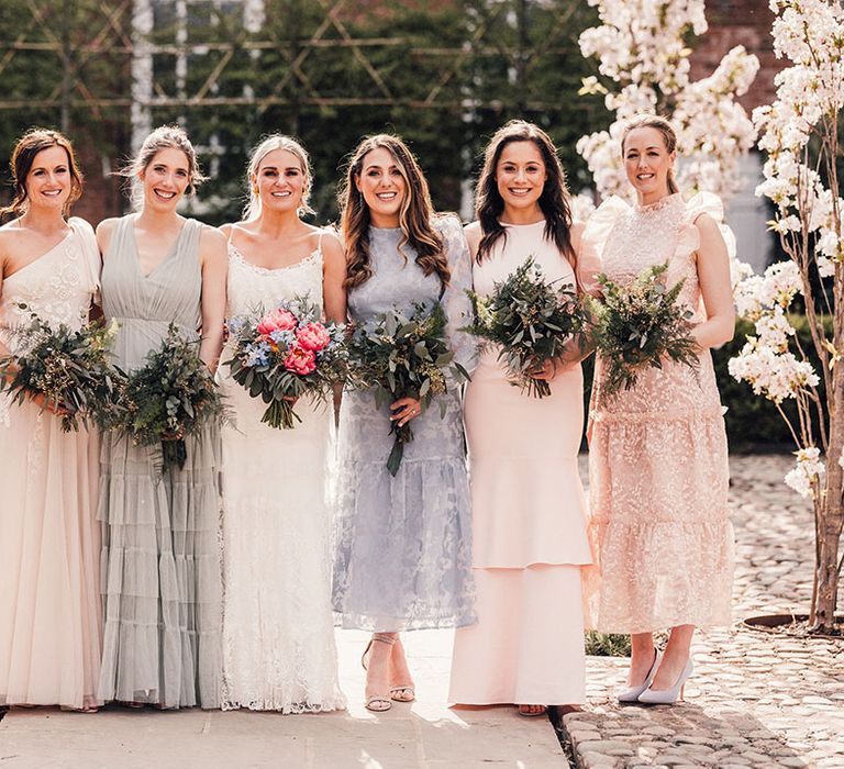 The bride stands smiling with the bridesmaids in ruffle and layered mismatched bridesmaid dresses 