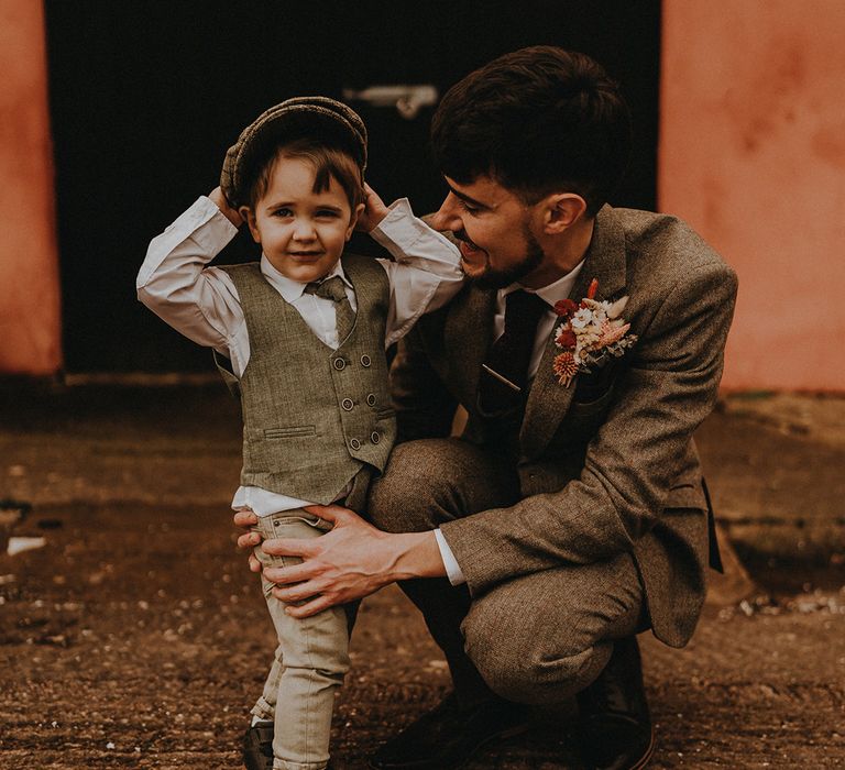 Page boy in matching shirt, trousers and flat cap with the groom in a grey suit with dried flower buttonhole 