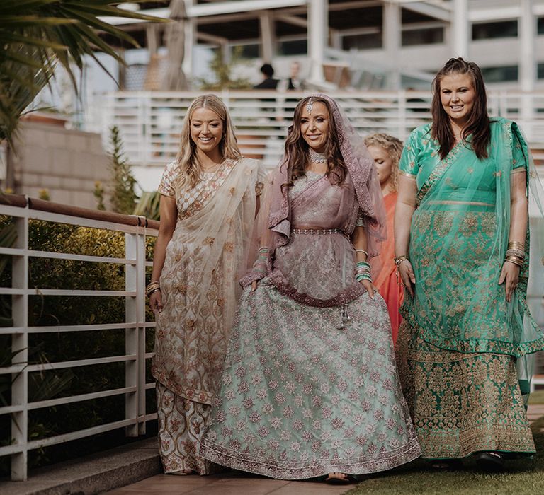 Bride in mint green and dusky pink ombre embellished lehenga walking with bridesmaids wearing mismatched bridesmaid lehengas 