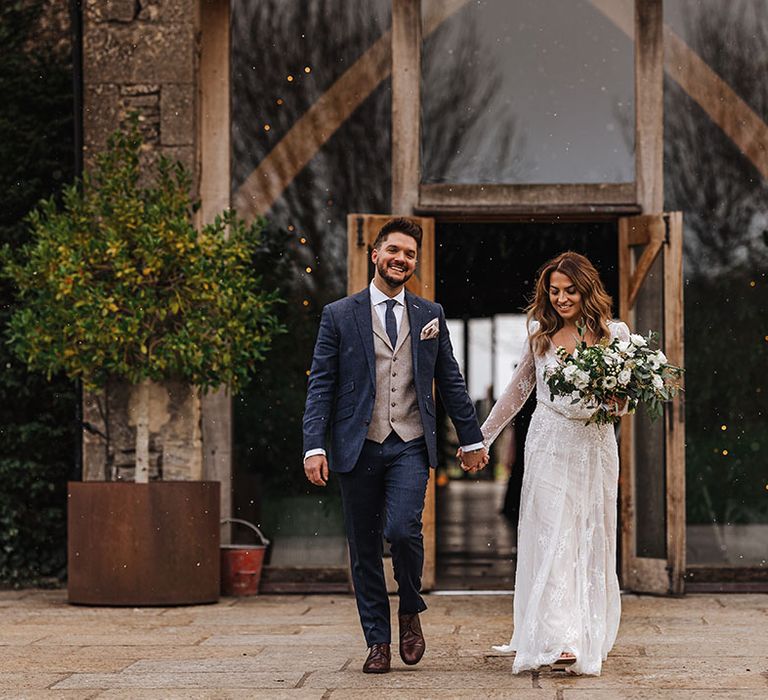 Bride and groom walk out of Stone Barn wedding venue together hand in hand 