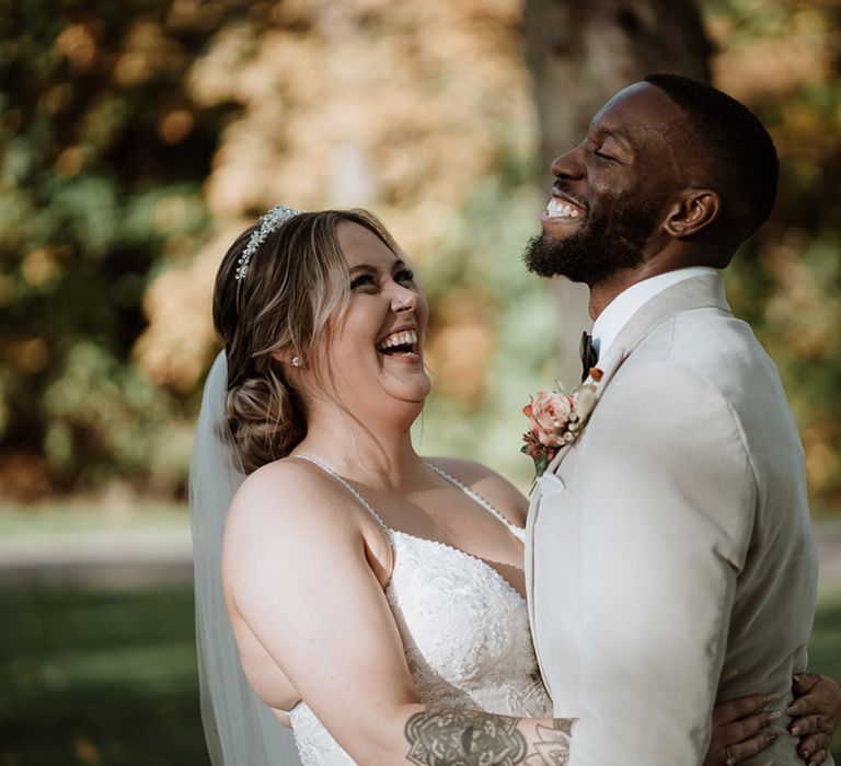 Laughing Black groom in a velvet light coloured suit jacket with the bride in a beaded wedding dress with tiara 