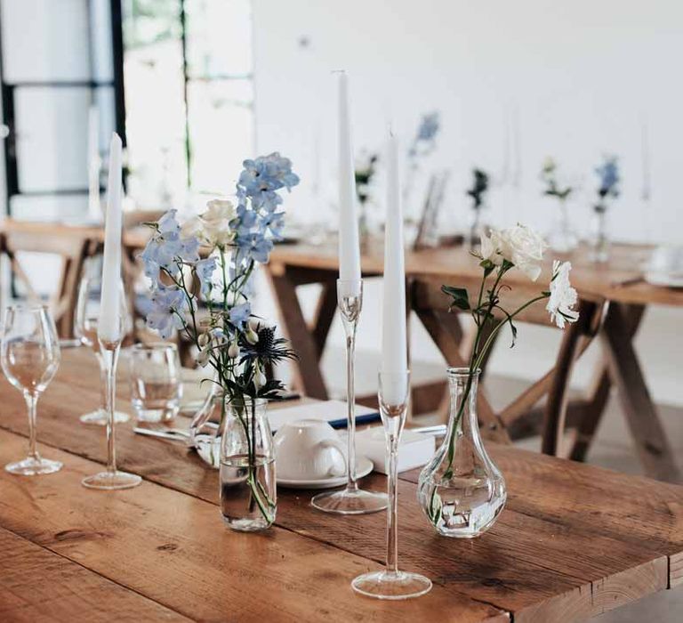 Modern rustic wedding tablescape at Brickhouse Vineyard Devon wedding with white garden rose and light blue delphinium wedding centrepieces and white tapered candles in glass candlestick holders