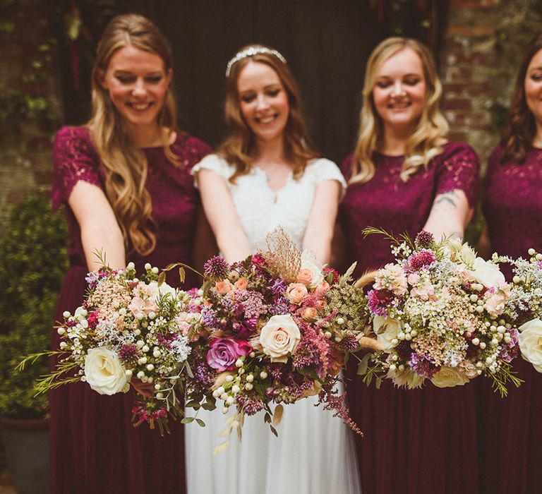 Gypsophila and rose wedding bouquets held by the bridal party in dark red bridesmaid dresses