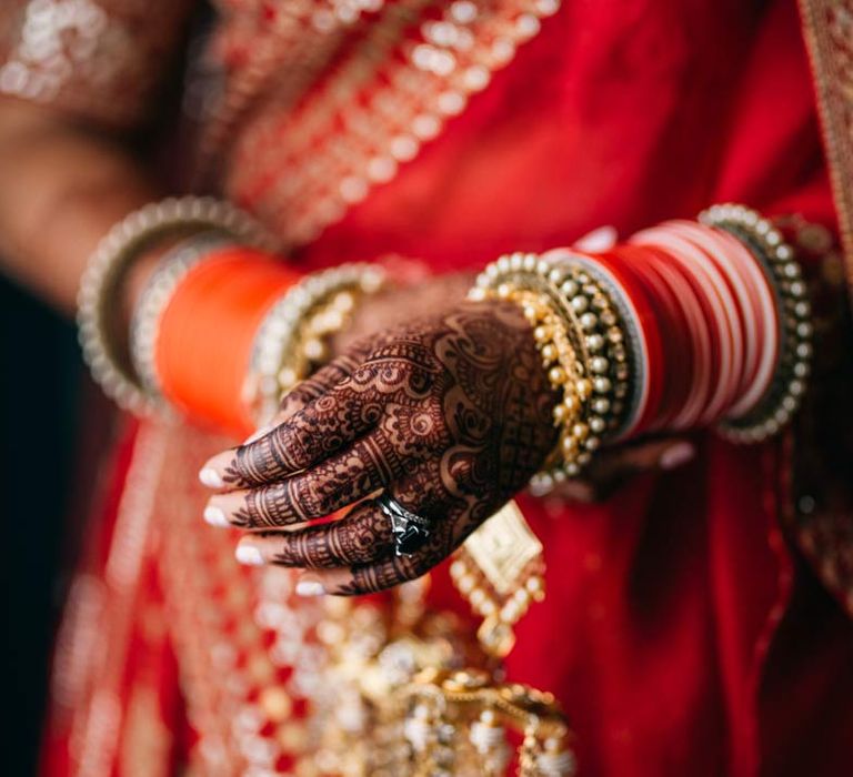 Bride in red and gold lehenga and gold and forest green bridal jewellery adorned with traditional Indian wedding henna on her hands 