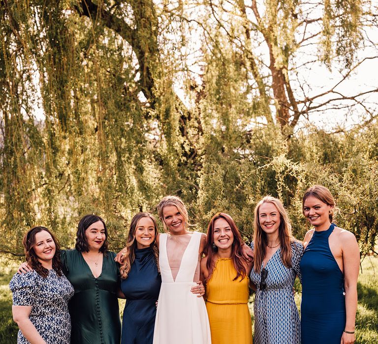 Bridesmaids in blue, yellow, and green mismatched bridesmaid dresses with the bride 