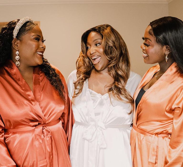 Bridesmaids in orange satin robes for autumn wedding with the bride as they get ready together 