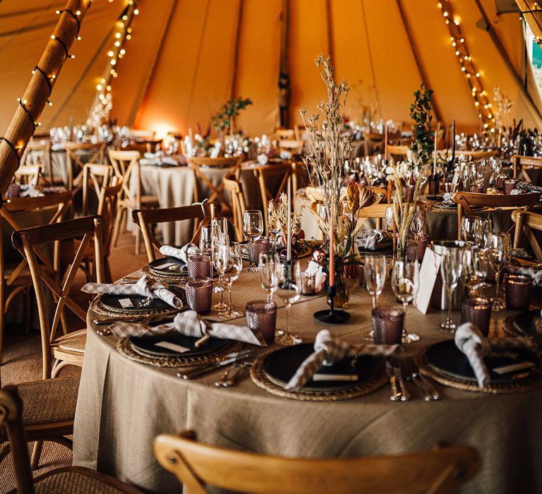 Tipi wedding reception with warm fairy lights and neutral decor with taper candles, checkered napkins and more 