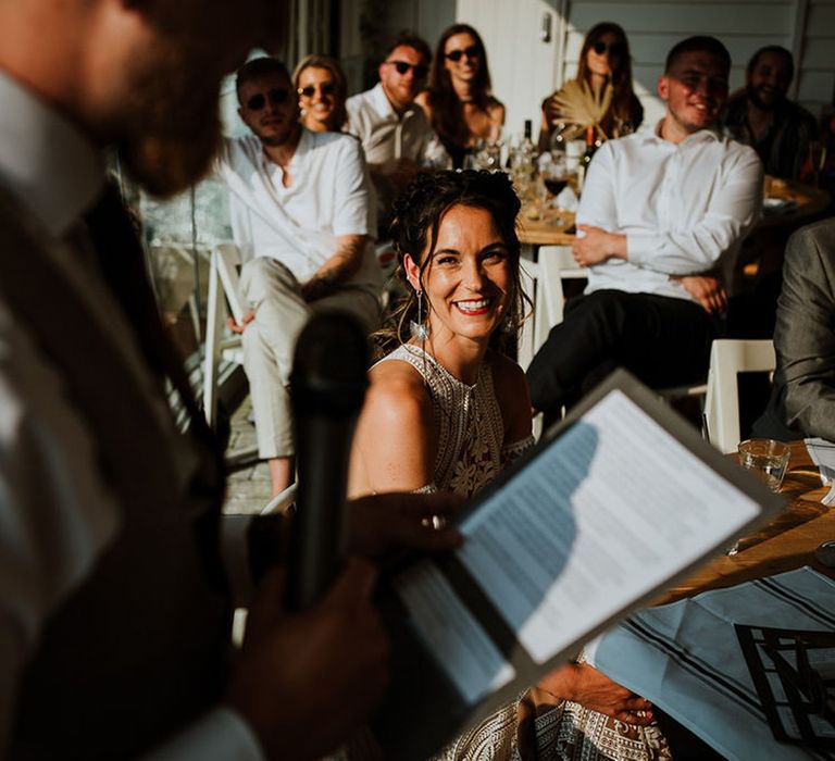 The bride laughs as she looks up at the groom reading his wedding speech 