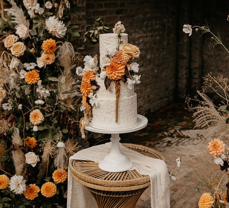 Three tiered white wedding cake with textured icing with orange dahlia flower cake decorations for safari wedding 