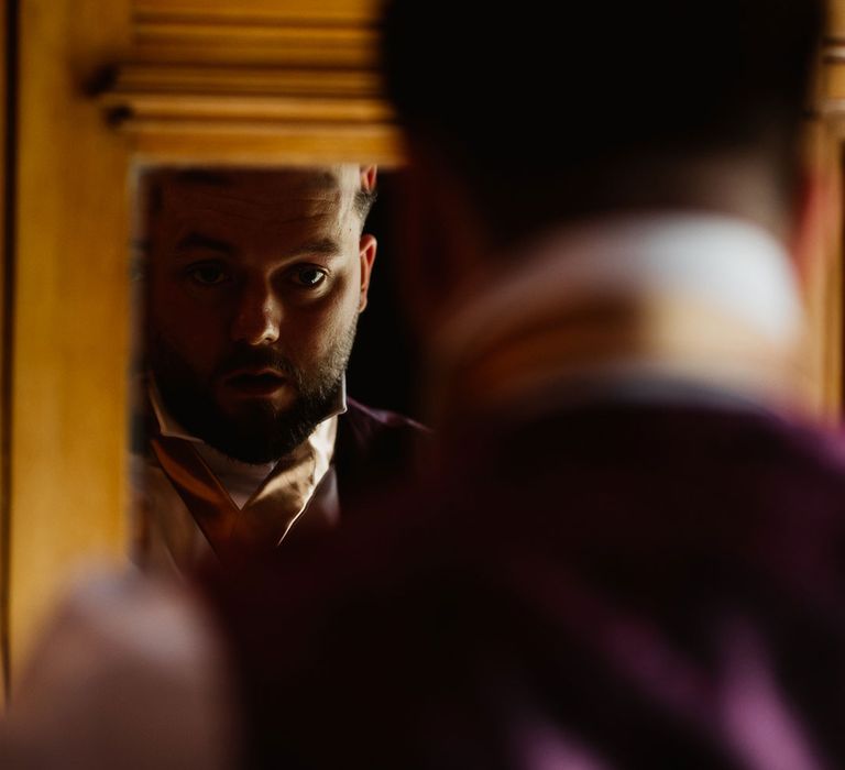 Groom looking at himself in mirror getting ready for wedding