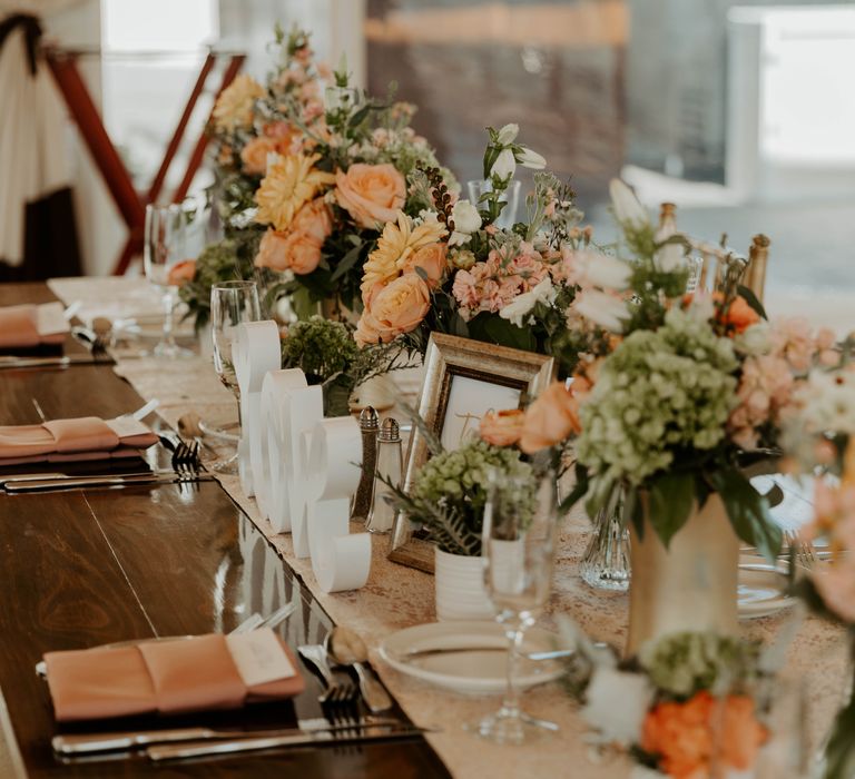 Gold table runner and blush pink and peach wedding flowers in vases 