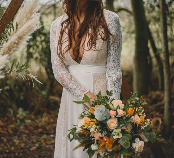 A bride with boho styling stands in a forest with loosely braided hair.