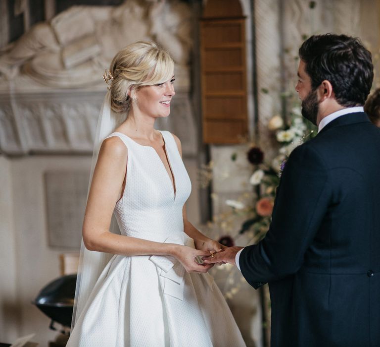 Bride in a Jesus Peiro wedding dress with bow waist detail exchanging vows with her husband at the church altar