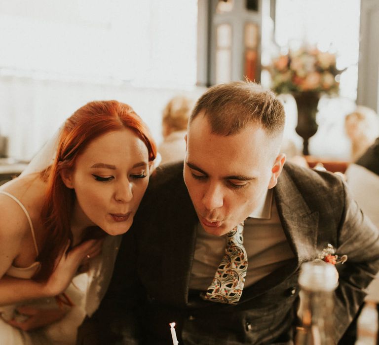 Bride and groom blowing out candle on small scone for London elopement wedding 