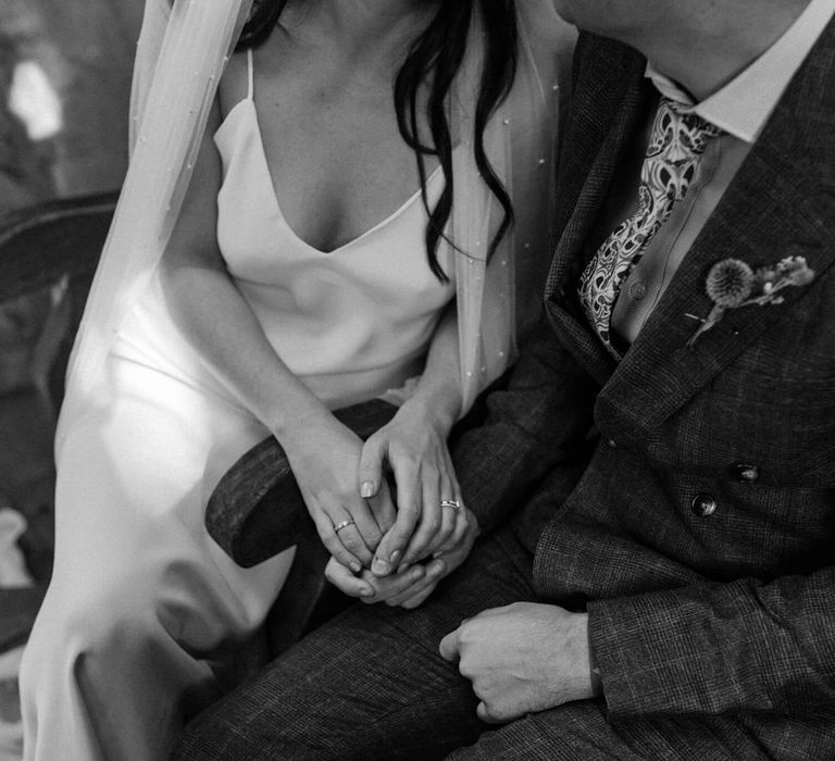 Close up shot of bride and groom holding each other bride wears simple silk wedding dress and groom wears check suit and patterned tie 