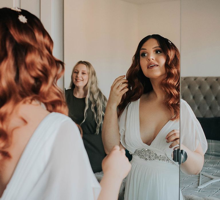 Bride with glam waves and celestial headband looks in mirror whilst getting ready