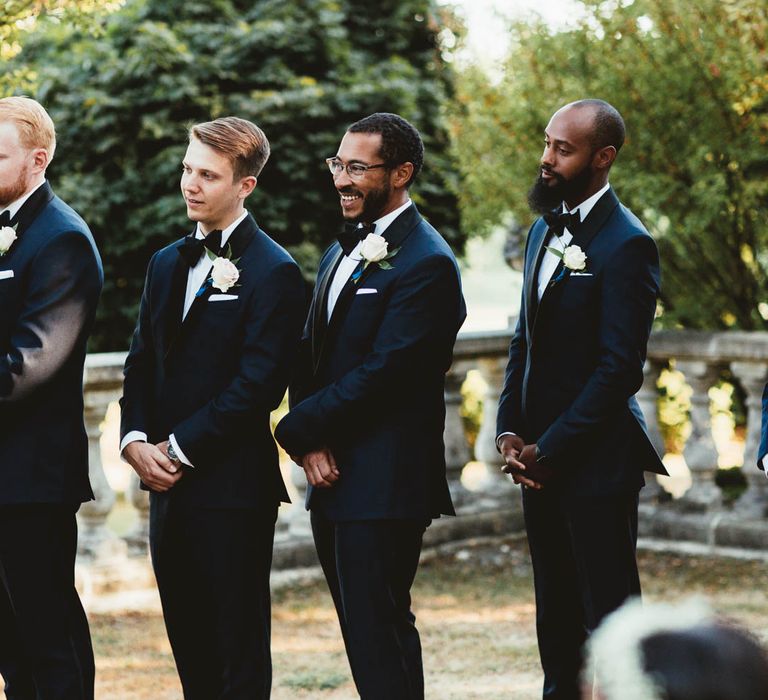 Groomsmen in navy suits with black lapels and bow ties wearing white rose buttonholes | Maryanne Weddings