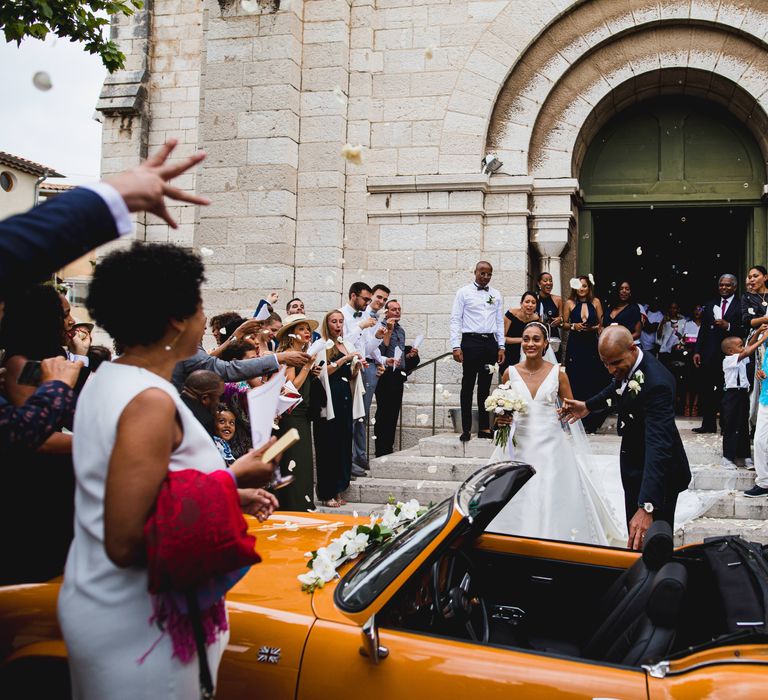 The bride and groom exiting the church in a vintage orange sports car