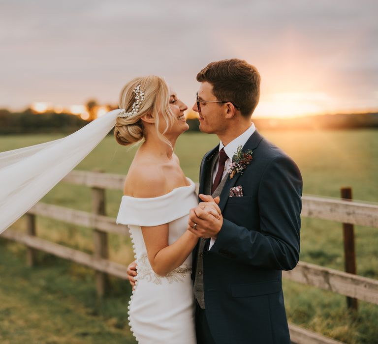 Bride & groom kiss as the sunsets and the brides veil blows in the wind