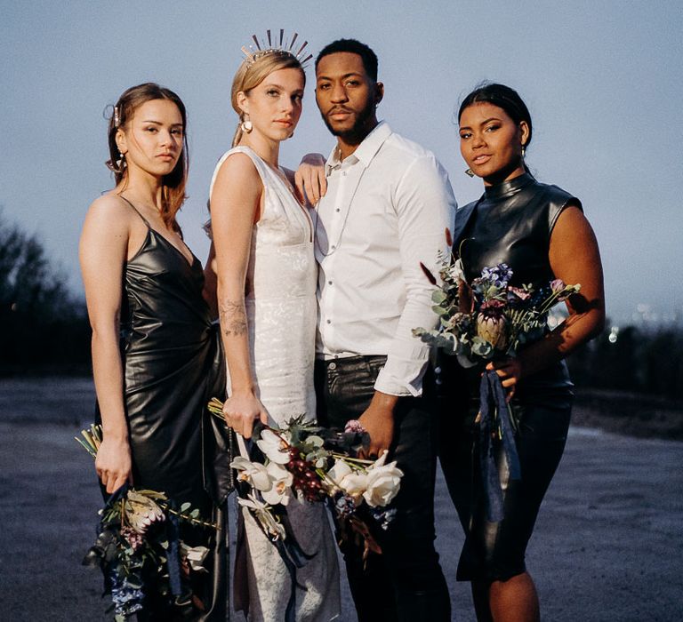 Wedding party portrait with bridesmaids in leather dresses, groom in leather trousers and bride in a jacquard midi dress and bridal crown. 