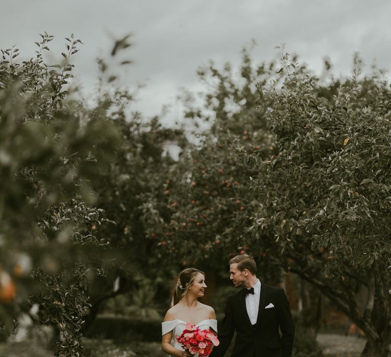 Bride & groom walk together whilst bride holds coral bouquet