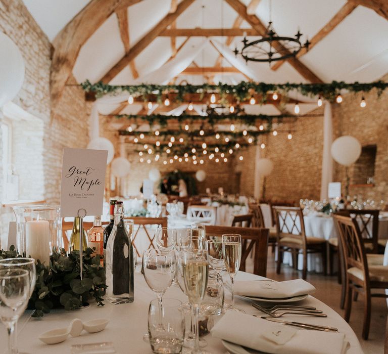 Stone barn wedding interior with beams, foliage, hanging pendant lights and white balloons