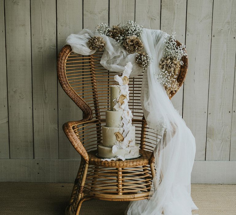 Buttercream wedding cake resting on a wicker chair with dried flower arrangements 