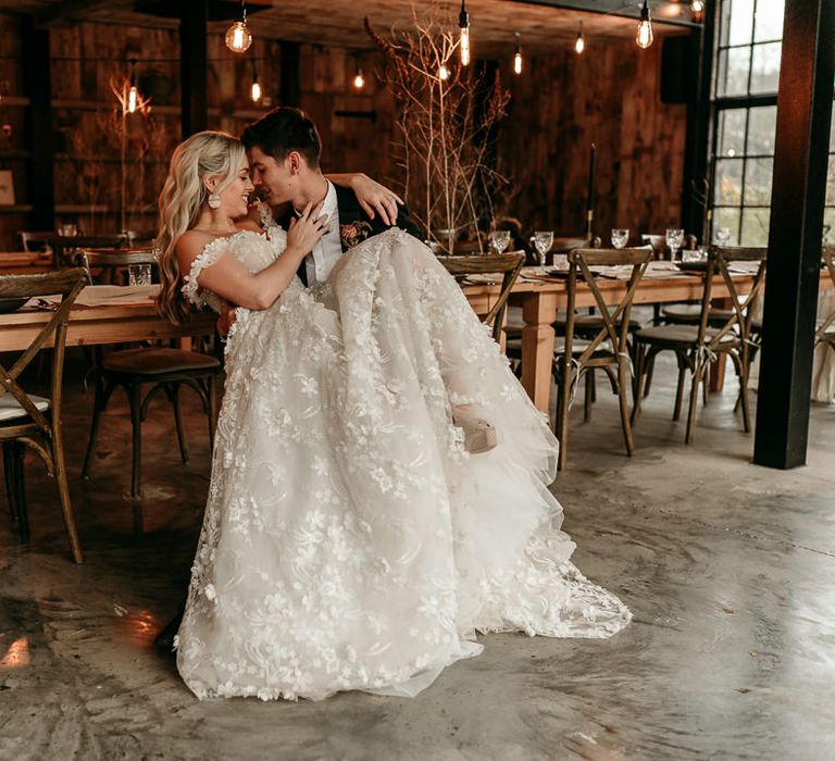 Bride in an appliqué lace wedding dress sitting on her husbands lap at the neutral wedding theme reception 