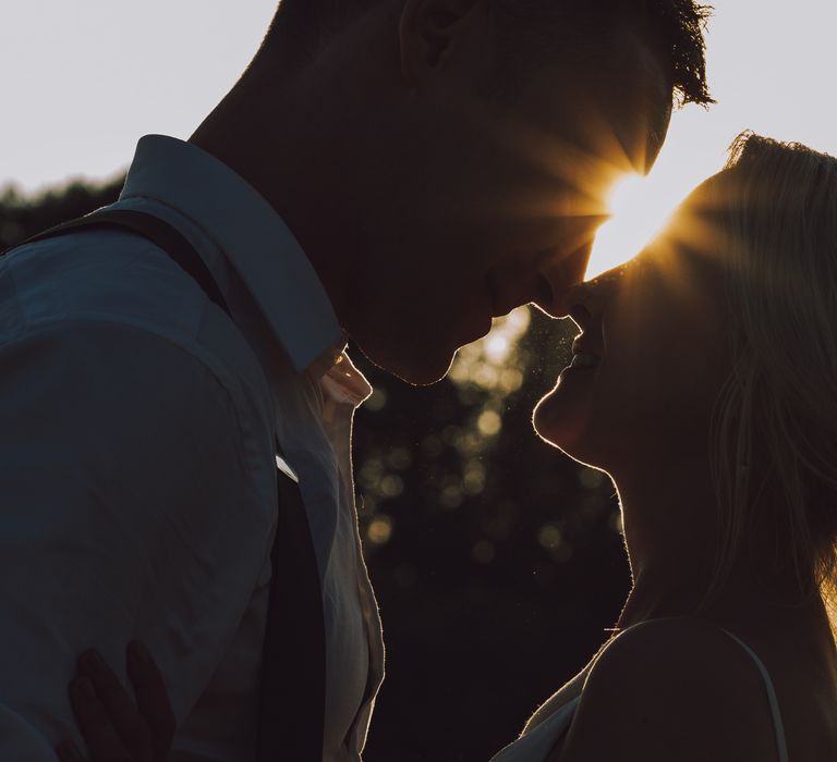 Bride & groom go in to kiss as the sun sets behind them