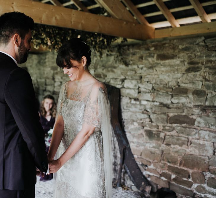 Bride and groom hold hands at their civil ceremony. The bride wears a sheer cape.