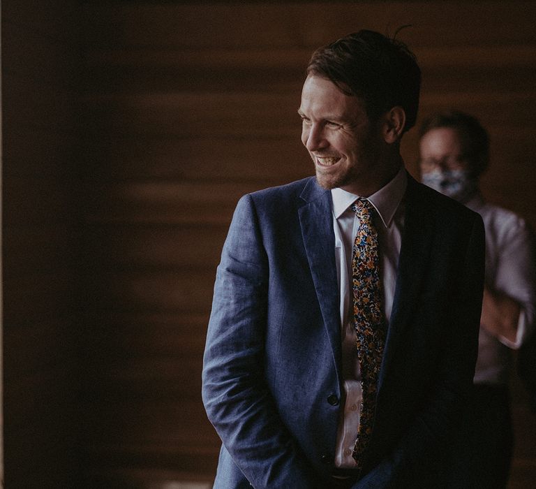 Groom smiles on the day of his wedding as he wears blue suit