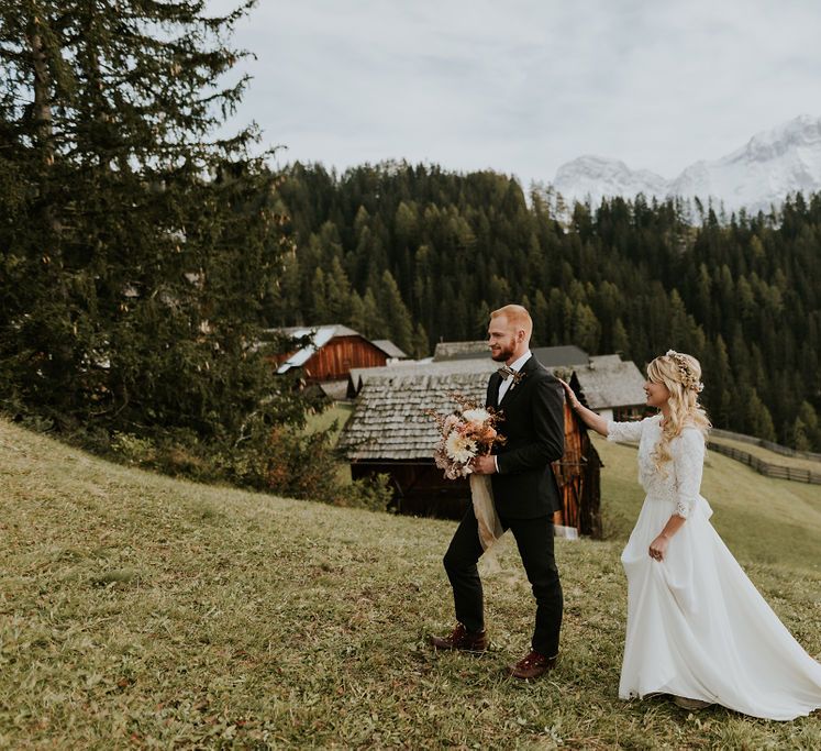 Bride in a Carla Spose wedding dress and flower crown approaching her husband holding an autumn wedding bouquet at their first look 