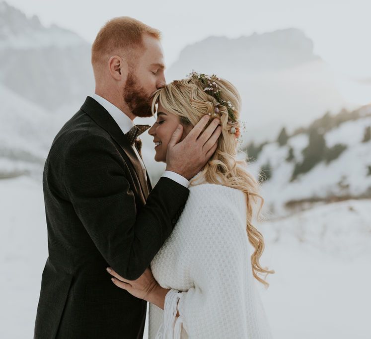 Groom in a dark check suit kissing his brides forehead at their intimate Dolomites wedding 