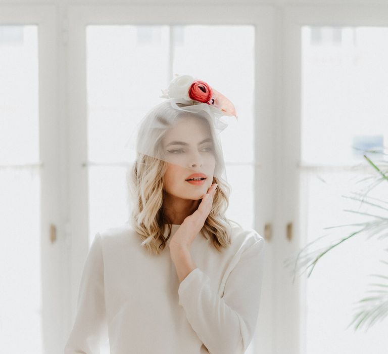 Bride wearing a long sleeve mid length wedding dress with sequin skirt detail, and a short mesh veil covering her face with flowers on her head