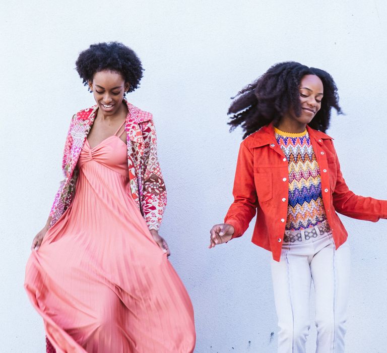 Bride-to-be in a coral dress and patterned coat with her partner in a patterned top and orange jacket 