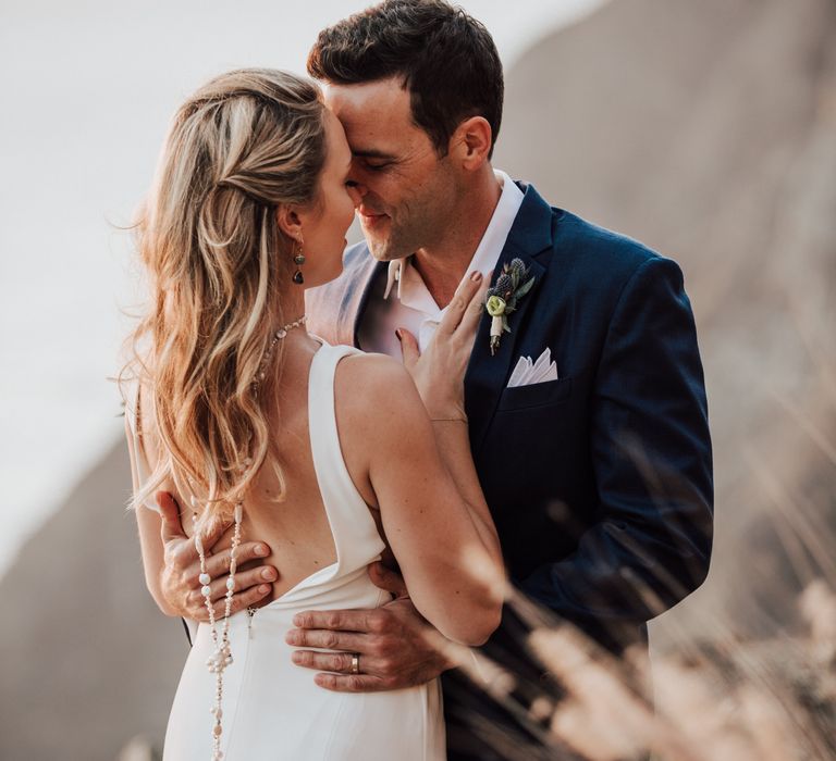 Bride & groom touch foreheads together on the cliffside as bride wears her hair in loose curls