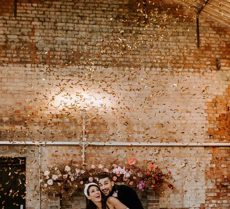 Bride and groom embracing under an explosion of gold confetti 