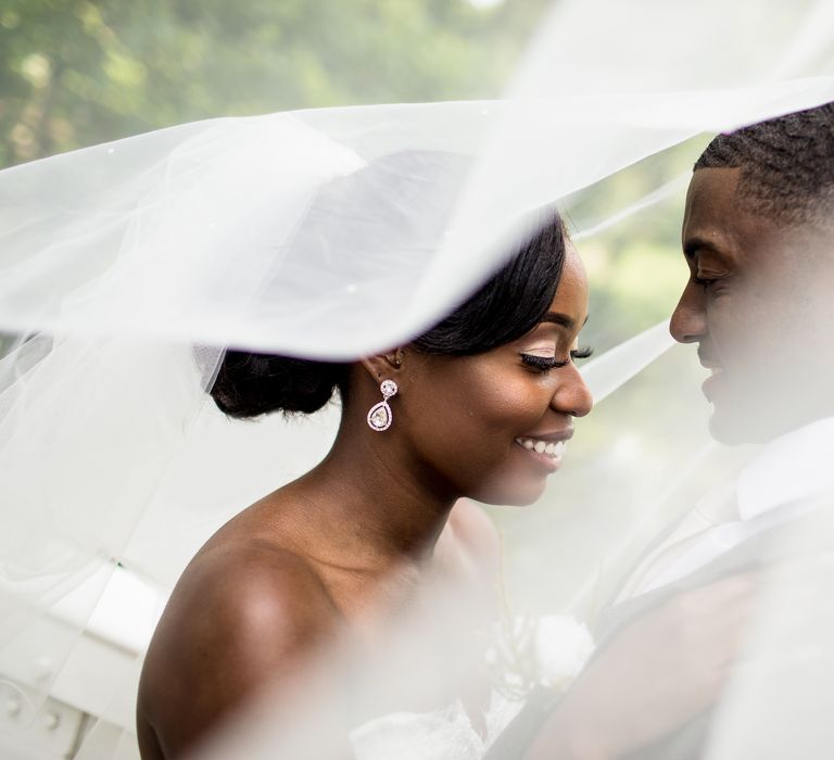 Bride & groom stand beneath veil as it blows in the wind