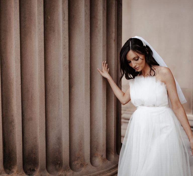 Pregnant bride wears ASOS wedding gown as she leans into pillar after wedding ceremony and wears her dark hair in loose curls