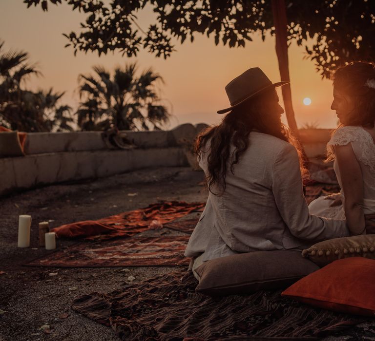 Bride & groom sit on rugs as they watch the sun set in the countryside of Sicily during their wedding day