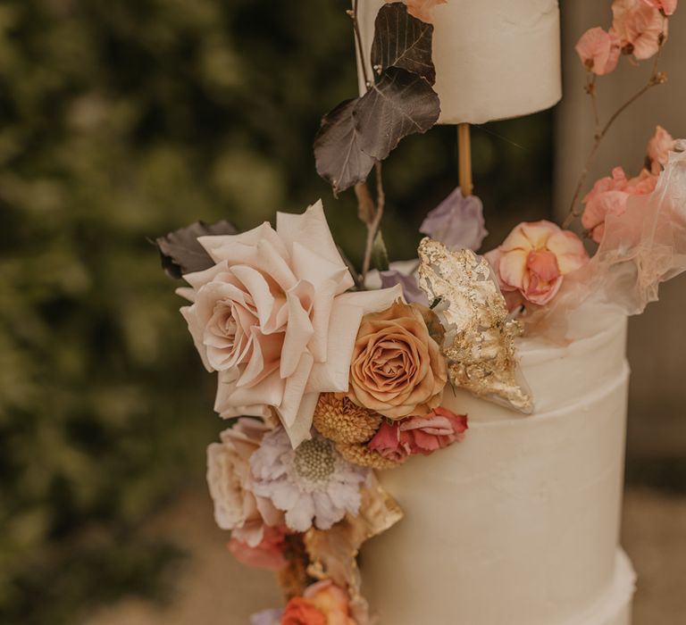 Buttercream wedding cake with elevated tier decorated in gold leaf and pastel wedding flowers 